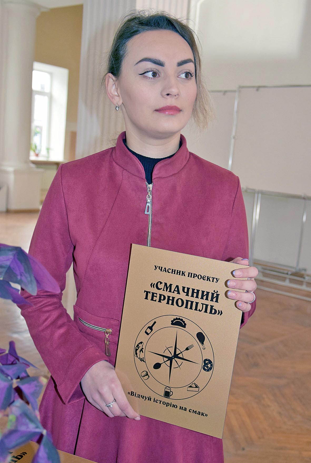 Керівниця Туристично-інформаційного центру м. Тернополя Ірина Потішна демонструє табличку, яку вручають учасникам проєкту «Смачний Тернопіль»